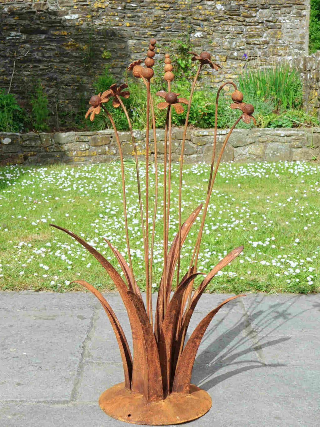 A rusty steel meadow composition - poppies, chamomiles, heleniums and reeds rising through tall grasses on a hand-formed domed base, on a garden path.
