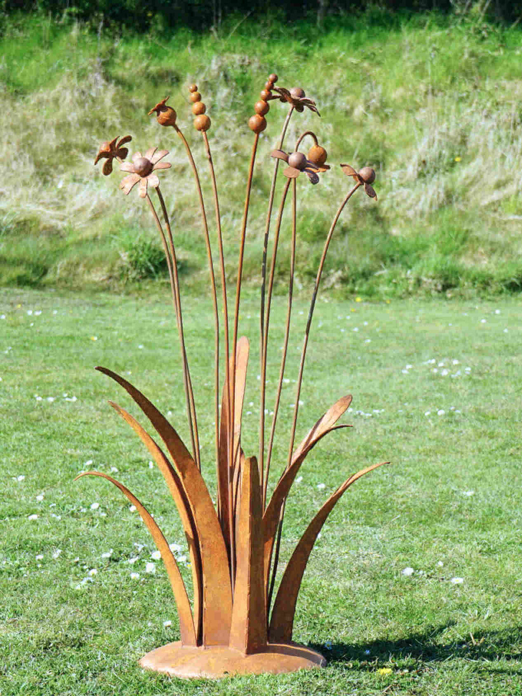 A rusty steel meadow composition - poppies, chamomiles, heleniums and reeds rising through tall grasses on a hand-formed domed base, on a grassy background