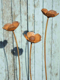 Three rusty metal buttercup sculptures against a wooden background