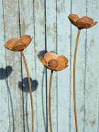 Three rusty metal buttercup sculptures against a wooden background