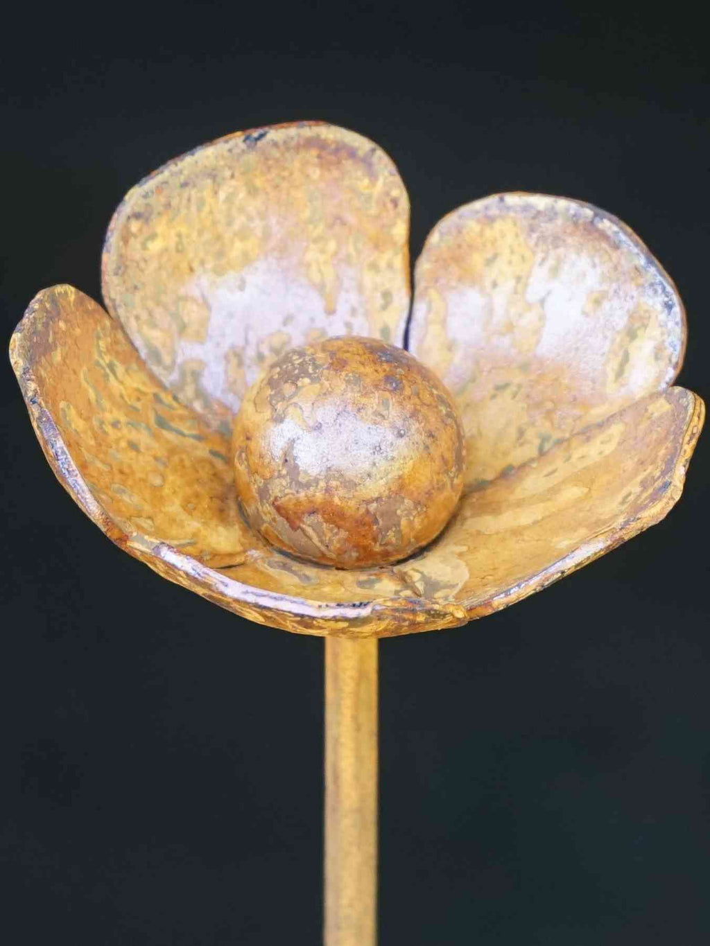 Close up image of rusty metal buttercup sculpture showing mottled patina finish