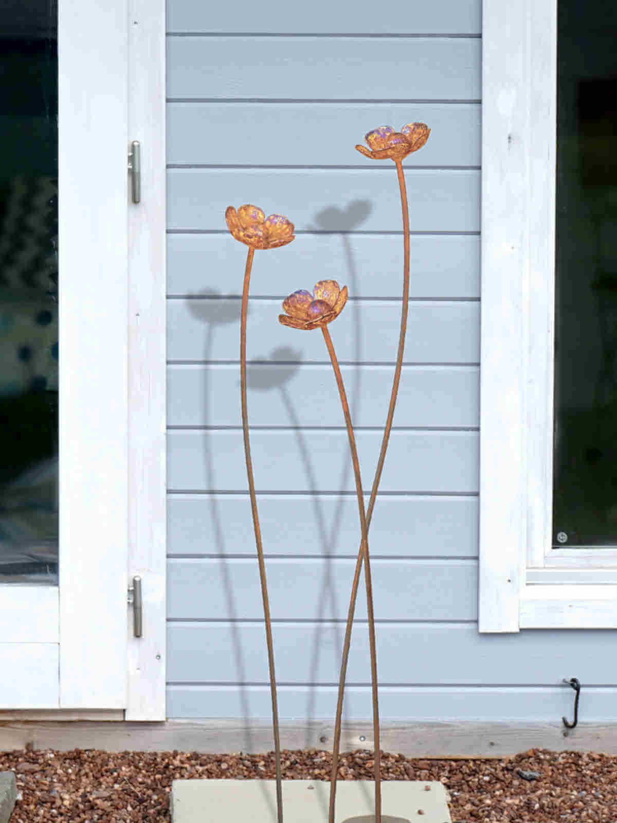 Three rusty metal buttercup sculptures against a light blue wall.