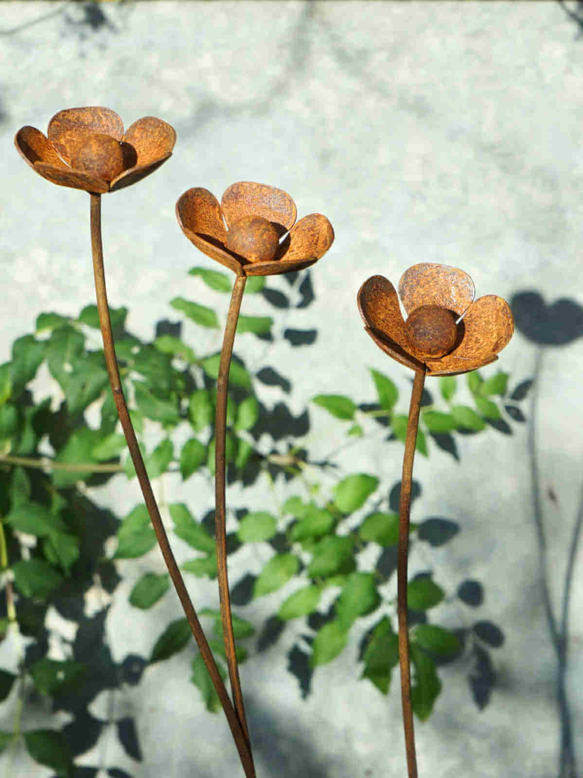 Three rusted metal buttercup sculptures against a blurred natural background