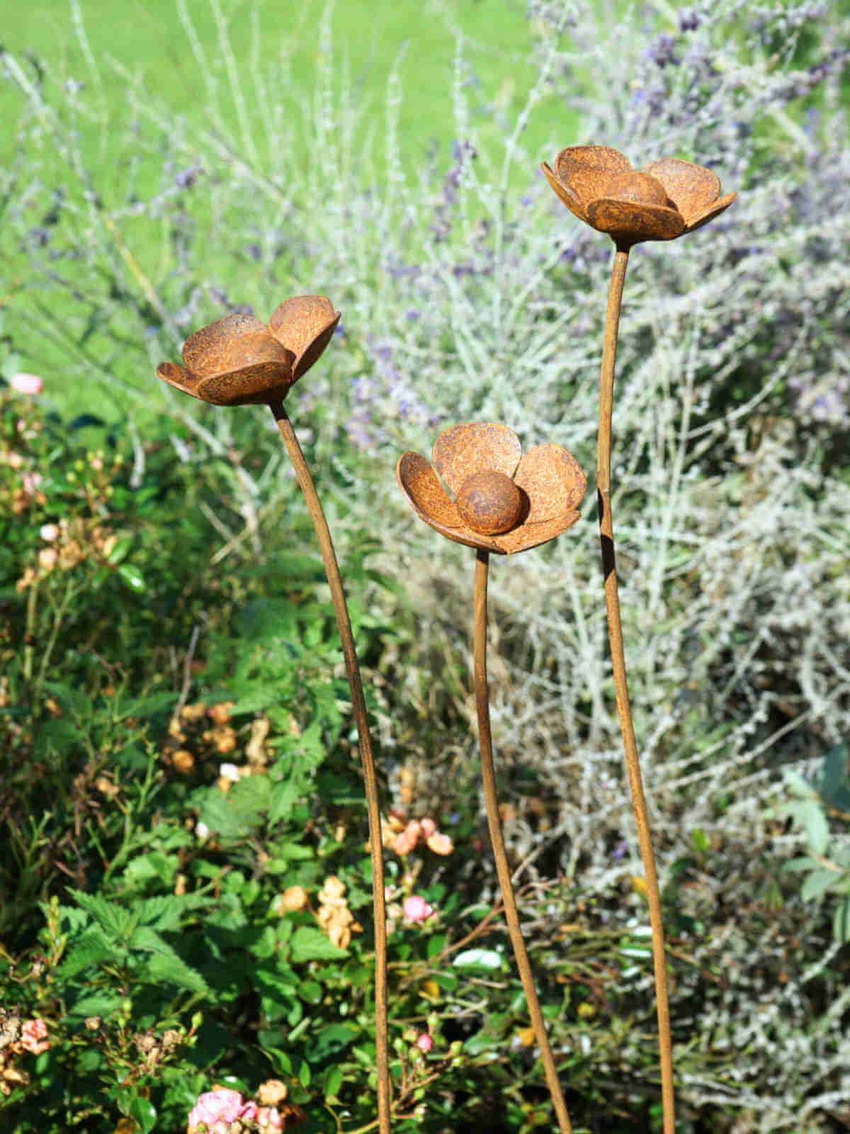 Metal buttercup sculptures in a garden setting with green and purple plants.