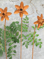 Three rusty metal Daffodil sculptures with green leaves against a textured wall.