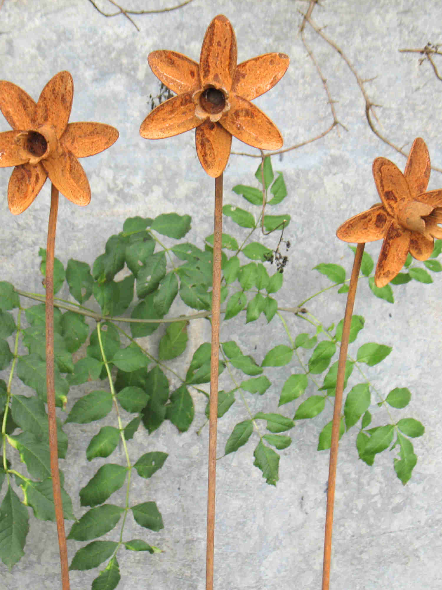 Three rusty metal Daffodil sculptures with green leaves against a textured wall.