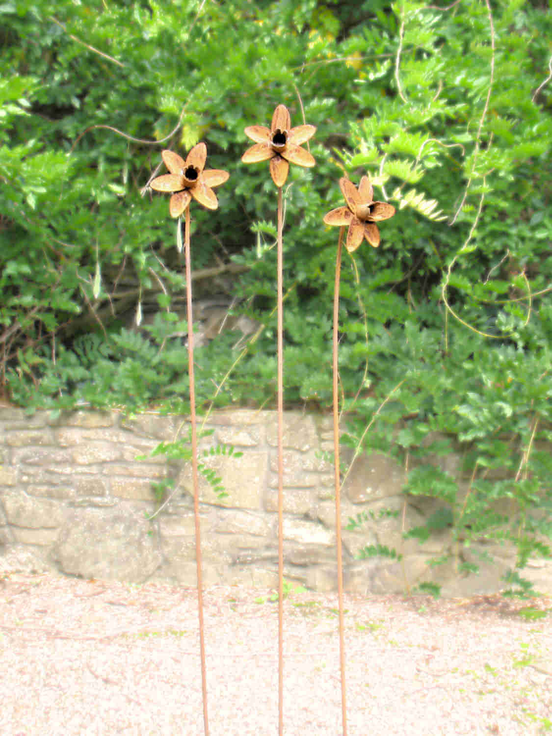 Rusty metal Daffodil sculptures against a green leafy background