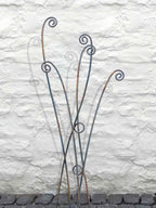 Rusty metal fern stems with intricate spiral tips against a textured stone wall