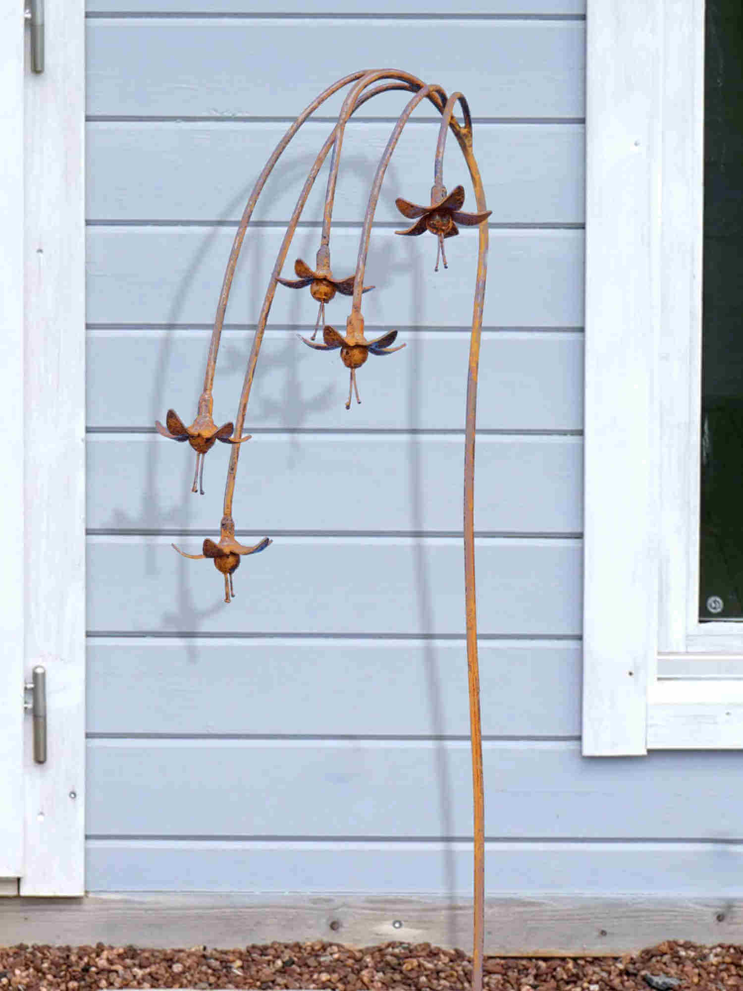 Rusty metal Fuchsias garden sculpture  against a light blue wall.
