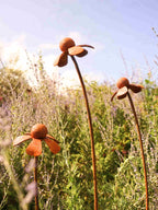 Rusty metal Heleniums flower sculptures in a garden setting with a clear blue sky.