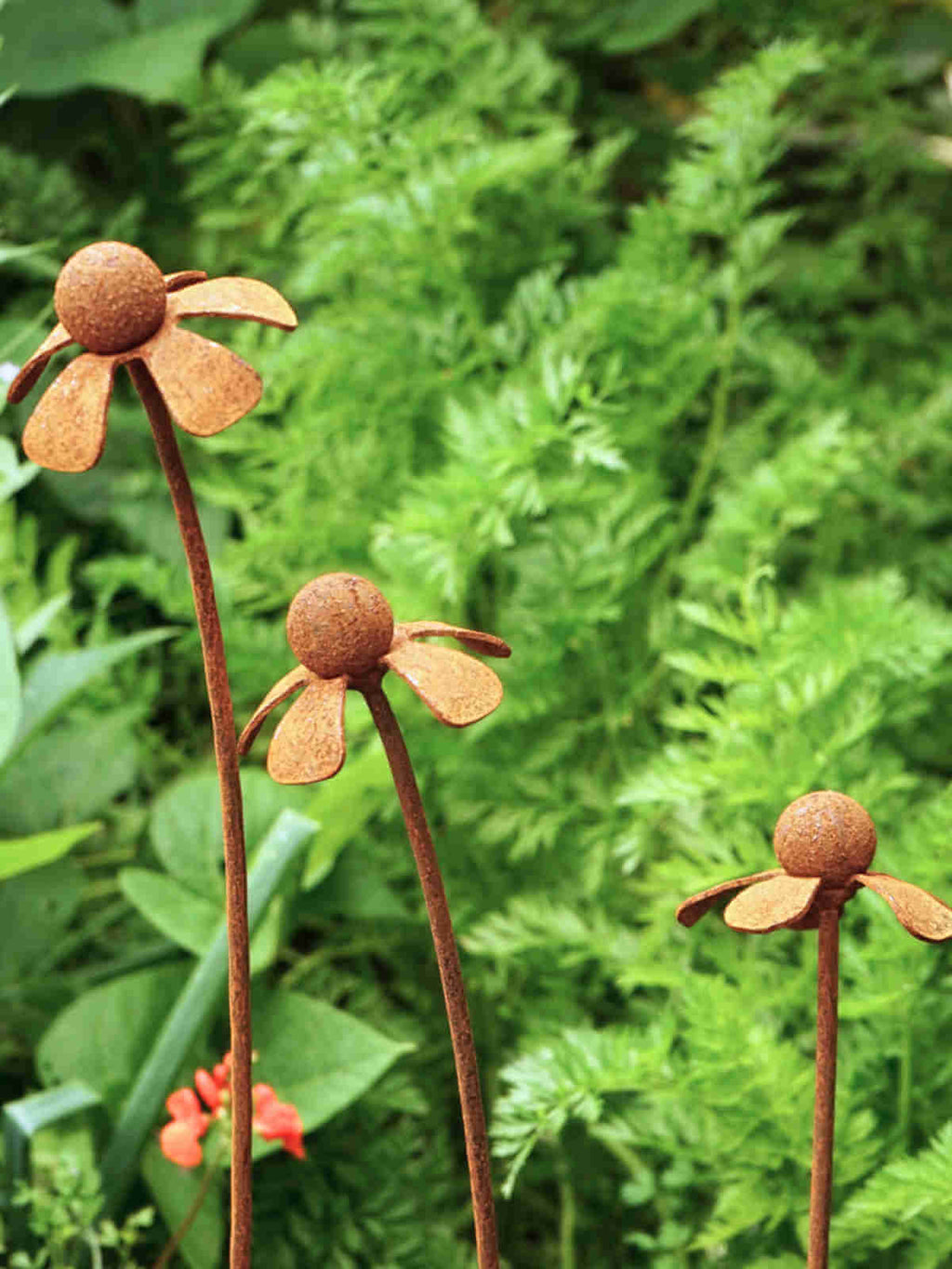 Rusty metal Heleniums flower sculptures among green foliage