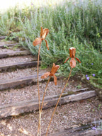 Rusty metal Iris flower sculptures on a wooden path with greenery in the background
