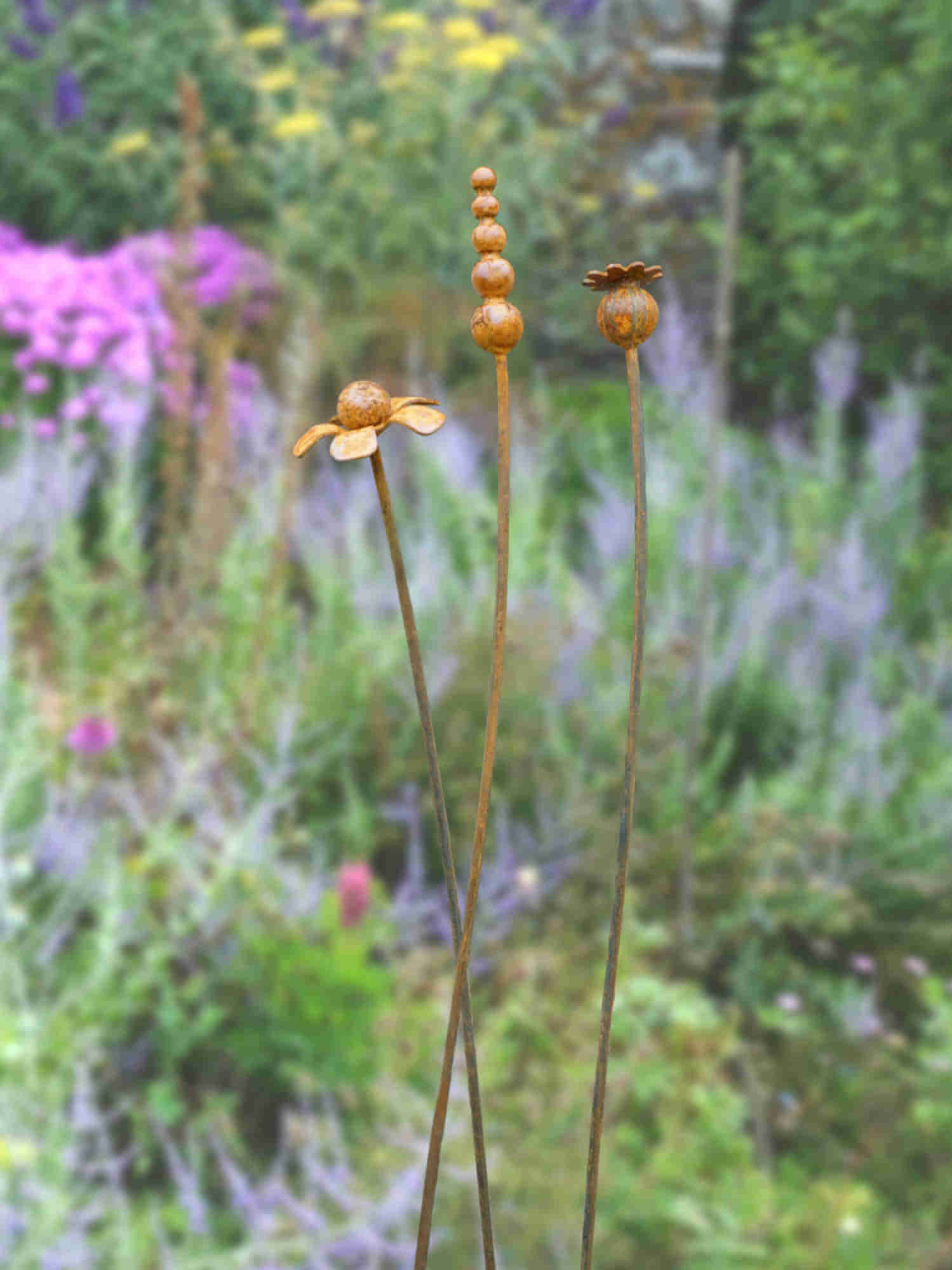Rusty metal mixed flowers sculptures in a garden setting with blurred background