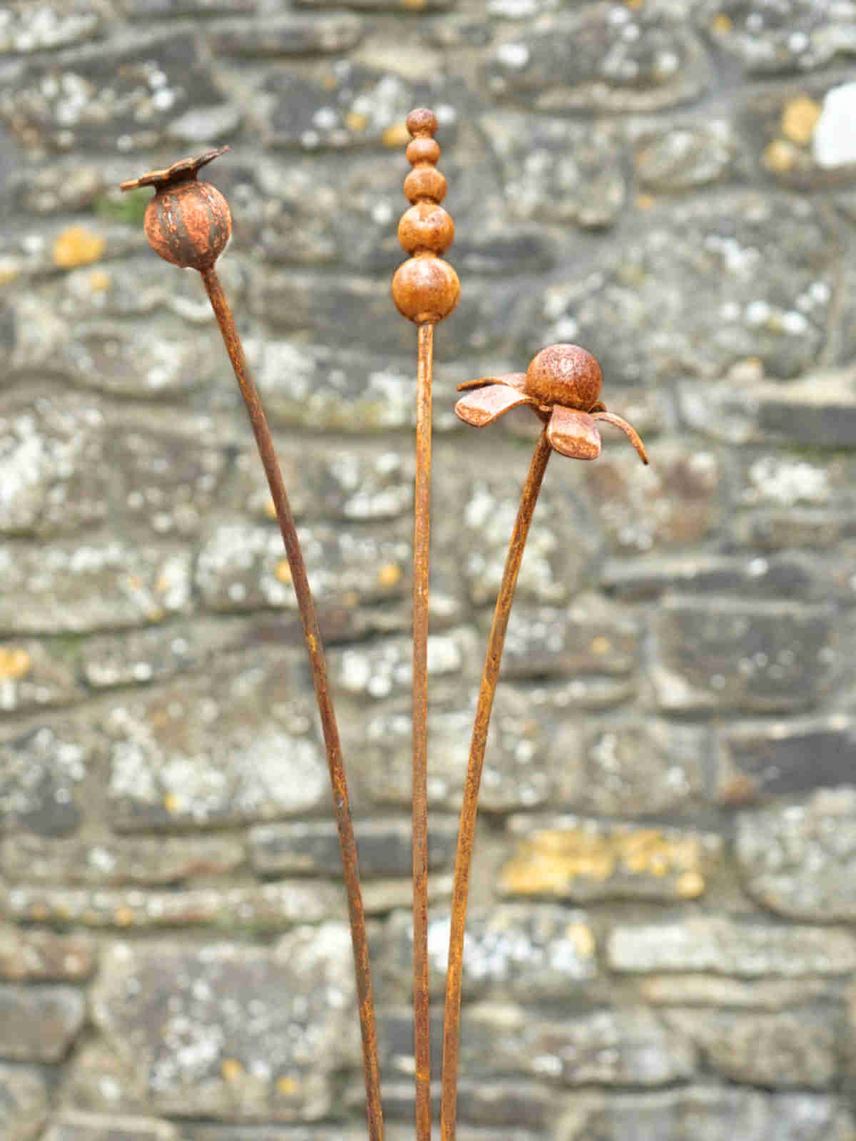 Rusty metal mixed flowers sculptures against a stone wall background