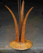 Close up image showing the mottled rusty patina of the tall grass stems, and the domed steel base.