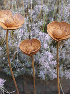 Three rusty metal Poppy sculptures in front of a lavender plant