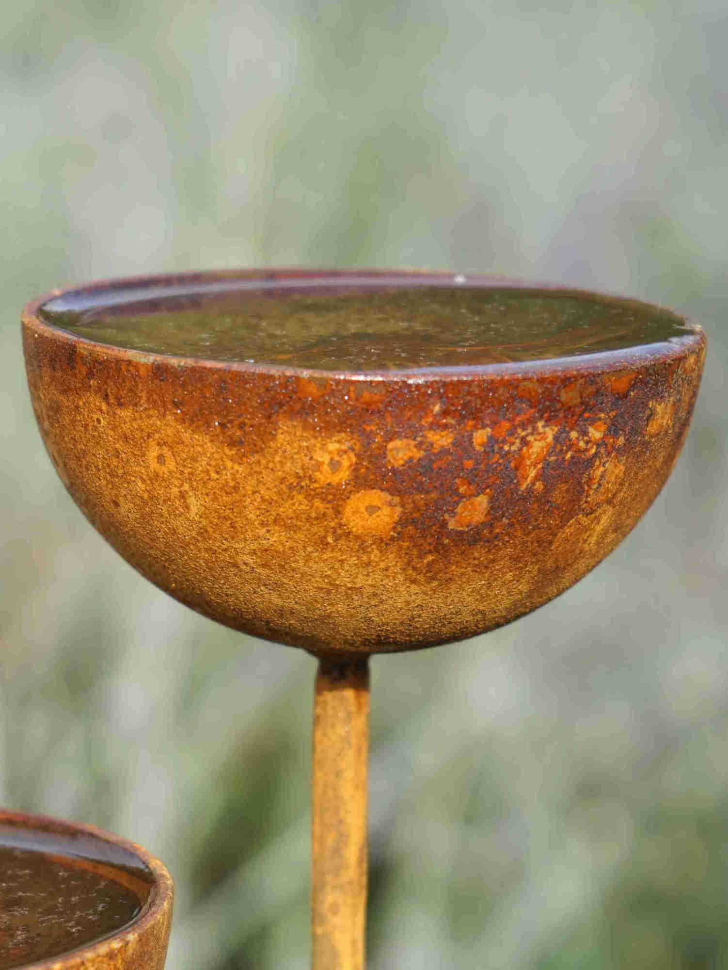 Close up image of a metal rain catcher showing the mottled rusty patina.
