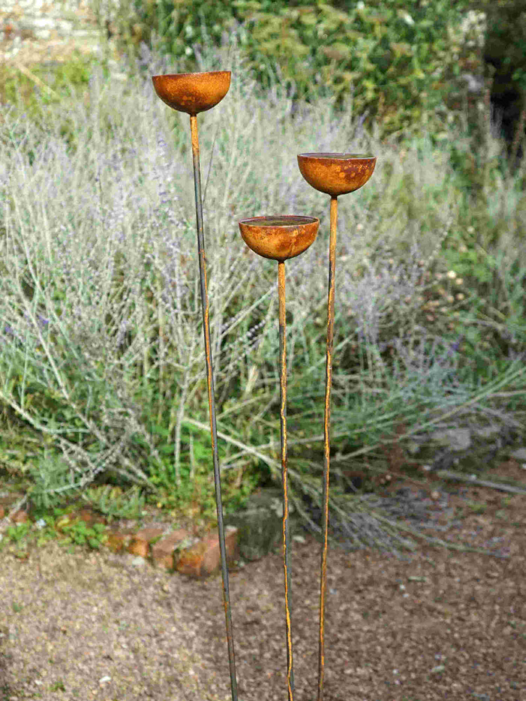 Three tall rusty metal rain catchers in a garden setting.