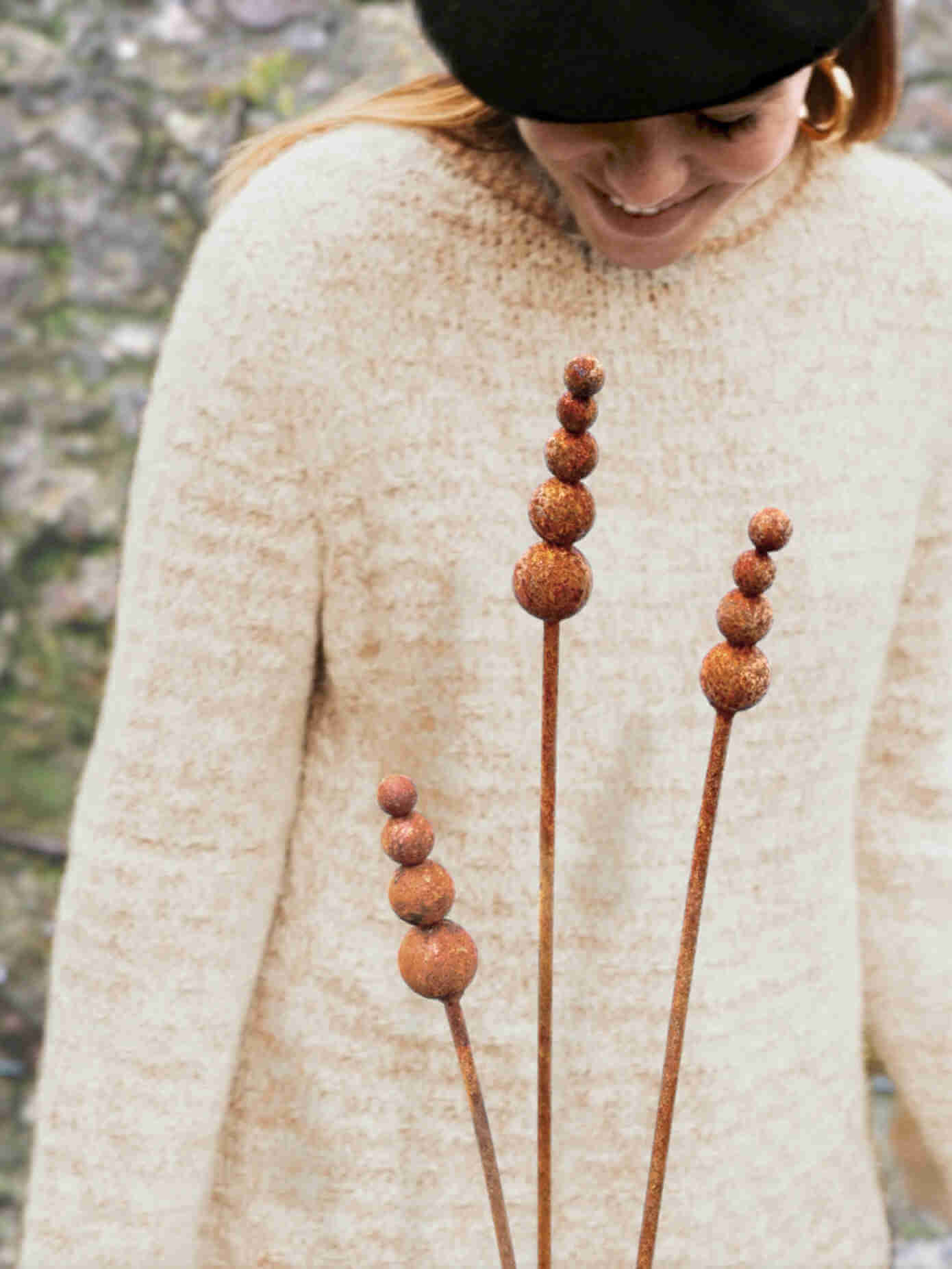 Rusty metal reed garden sculptures with a young woman wearing a beige sweater in the background