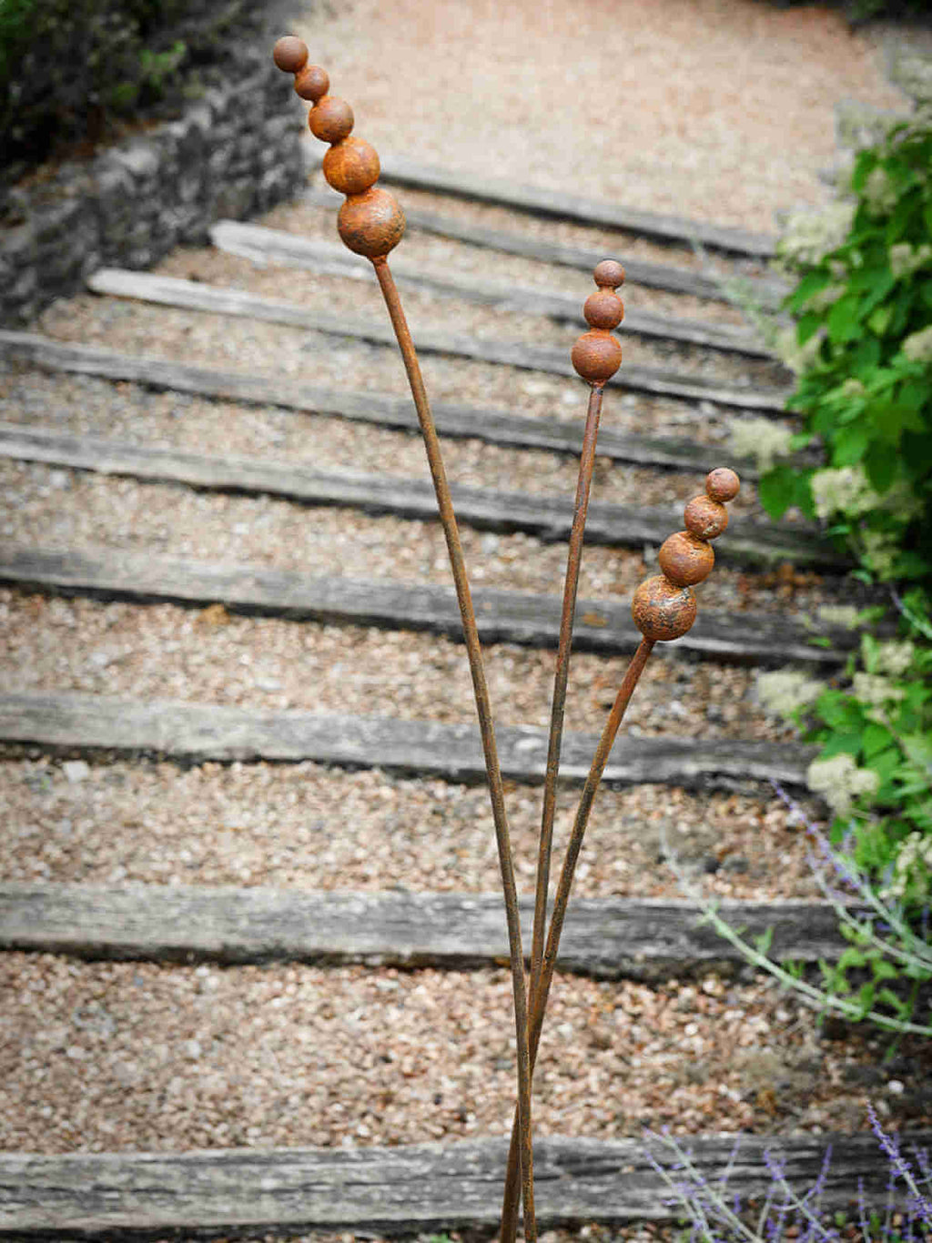 Rusty metal reed garden sculptures on a gravel path background