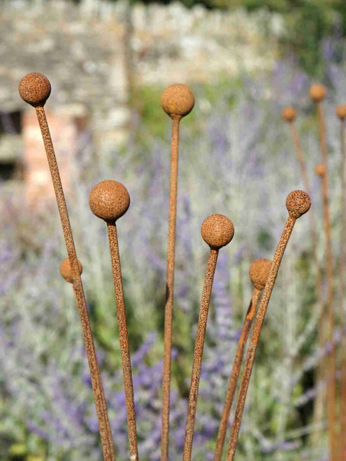 Rust-colored plant stakes with spherical ends against a blurred natural background