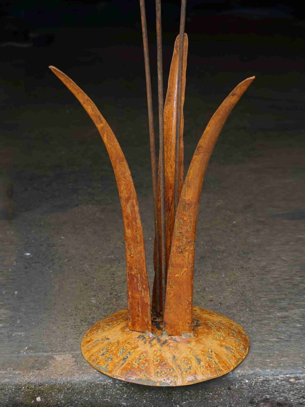Close up image showing the mottled rusty patina of the tall grass stems, and the domed steel base.