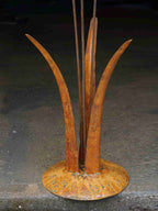 Close up image showing the mottled rusty patina of the tall grass stems, and the domed steel base.
