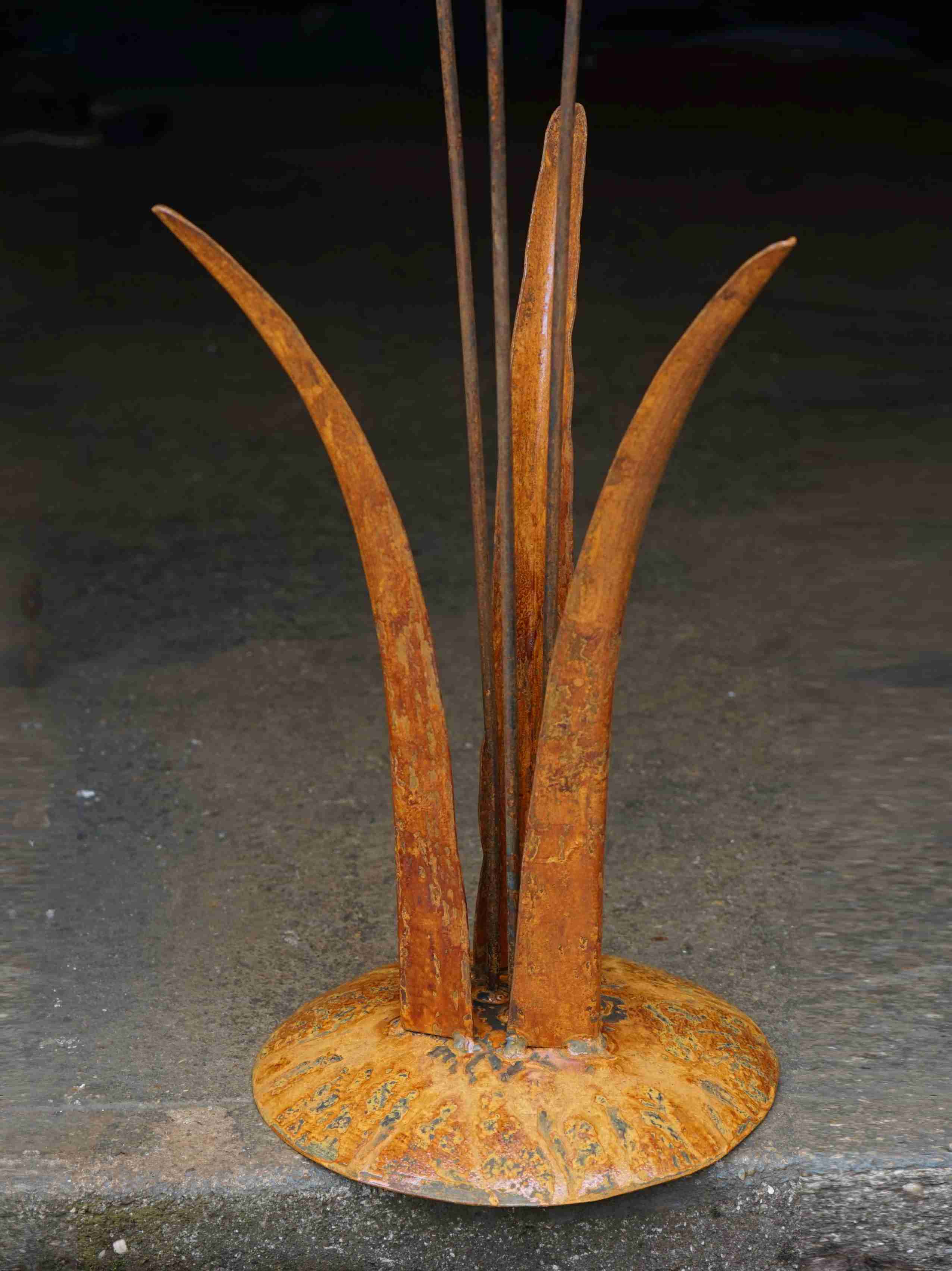 Close up image showing the mottled rusty patina of the tall grass stems, and the domed steel base.